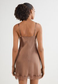 Brun satin slipklänning med tunna spaghetti-remmar och spetsdetaljer i fållen. Slät textur, figurnära passform och låg ryggdesign.