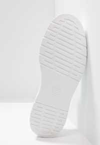 Sola di sneaker bianca con scanalature e motivi testurizzati. Presenta una punta rotonda e una forma piatta, realizzata in materiale simile alla gomma.