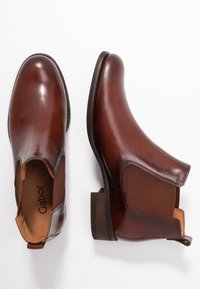 Botas de tobillo de cuero marrón oscuro con paneles laterales elásticos, un acabado suave, un tacón bajo apilado y detalles de costura sutiles. Marca Gabor en el interior.