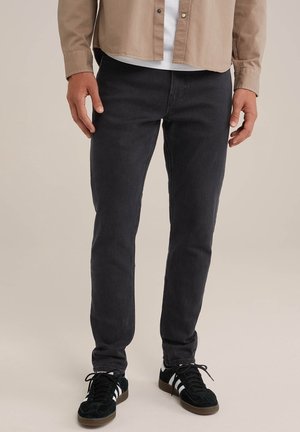 Jeans ajustados de mezclilla en gris oscuro, con un diseño clásico de cinco bolsillos, combinados con zapatillas negras con rayas blancas.
