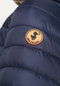 Marine pufferjack met een ronde oranje patch met een zwart eendenlogo en de tekst "SAVE THE DUCK", die een gequiltde textuur laat zien.