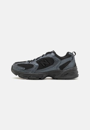 Sort og mørkegrå atletisk sneaker med mesh-stof, snørebånd, tyk sål og en trækkeøjle på hælen.
