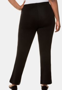 Pantaloni neri elasticizzati con vestibilità slim e fondo svasato. Presentano una cintura liscia e una consistenza morbida, progettati per il comfort e la libertà di movimento.