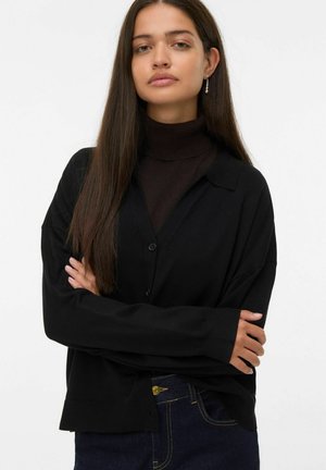Zwarte cardigan met een knoopsluiting, kraag en lange mouwen. Draag het over een donkere turtleneck, met een ontspannen pasvorm en een zachte textuur.