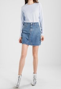 Haut à manches longues bleu clair associé à une mini-jupe en denim. La jupe présente une coupe asymétrique et une fermeture à bouton sur le devant. Bottines argentées.