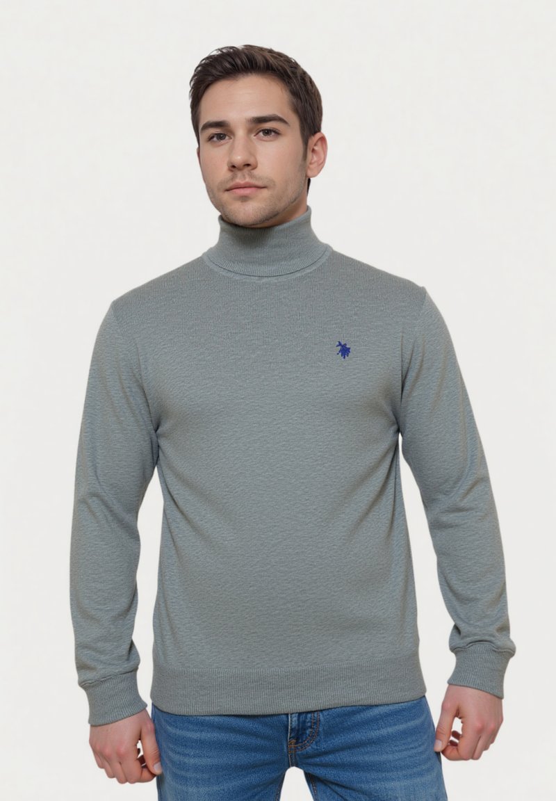 Hellgrauer Rollkragenpullover mit strukturiertem Muster, gerippten Bündchen und Saum. Verfügt über ein kleines blaues Logo auf der Brust. Getragen mit blauen Jeans.