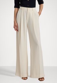 Crème wijde beenbroek met een zachte textuur, voorzien van een hoge taille, plooien aan de voorkant en zijzakken. Gestyled met een zwarte top en bruine schoenen.