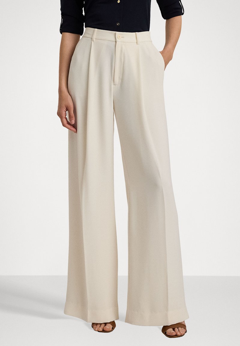 Crème wijde beenbroek met een zachte textuur, voorzien van een hoge taille, plooien aan de voorkant en zijzakken. Gestyled met een zwarte top en bruine schoenen.