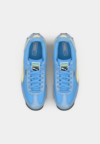 Tenis de camurça azul com detalhes amarelos, bico redondo, atacadores planos e sola preta. Possui uma etiqueta com logo na língua e marcação lateral.