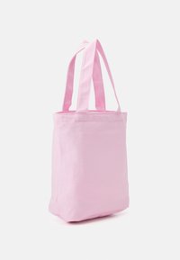 Bolso tote suave en color rosa, hecho de tela, con dos asas largas, de pie sobre un fondo blanco liso.