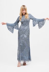 Długa niebieska wieczorowa sukienka z dzwonowymi rękawami, ozdobiona srebrnymi koralikami i skomplikowanymi wzorami. Przezroczysta warstwa z płynącą sylwetką.