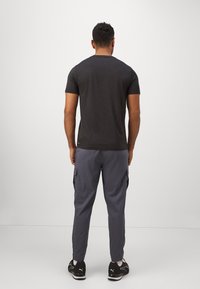 Heren fitted grijs t-shirt, gecombineerd met donkergrijze cargobroek met zijzakken. Schoenen zijn zwart met witte accenten.