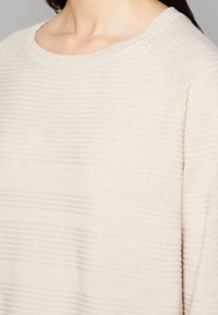 Pull beige clair en maille texturée à côtes, avec un col rond et des manches raglan, fabriqué dans un tissu tricot doux.