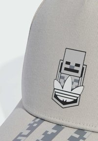 Szara czapka z teksturowanej tkaniny z czarno-białym graficznym logo. Projekt zawiera wzory w kamuflażu na daszku oraz zaokrągloną koronę.