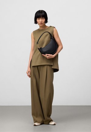 Borsa a mezzaluna in pelle nera con silhouette curvata, hardware dorato e manico corto, tenuta da una persona in un outfit verde oliva.