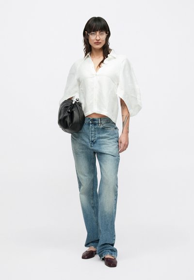 Λευκό κοντό τοπ με φουσκωτά μανίκια, ανοιχτό μπλε τζιν παντελόνι και μαύρη δερμάτινη τσάντα. Το μοντέλο φορά καφέ παπούτσια και διαφανή γυαλιά.