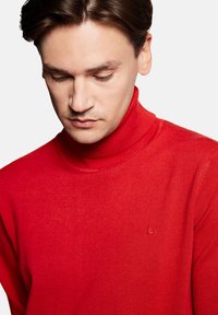 Czerwony sweter z golfem, wykonany z miękkiego materiału. Posiada prążkowany kołnierz i mały detal z logo na piersi. Gładka faktura.