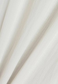 Tessuto bianco con sottili righe verticali testurizzate e morbide pieghe che creano un delicato motivo a onde.