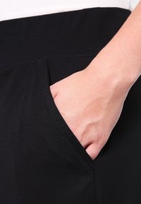 Svarta stretchbyxor med sidoficka, med en slät textur och prydlig sömnad längs midjebandet och ficköppningen.