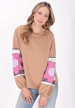 Lysbrun langærmet bluse med pink blomsterdesign på ærmerne, med en rund hals og elastiske manchetter. Sættes sammen med lysblå jeans.