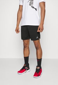 Men's athletic outfit featuring a white graphic t-shirt, black mesh shorts, and black sneakers with red accents and logo.