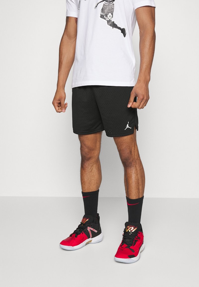 Men's athletic outfit featuring a white graphic t-shirt, black mesh shorts, and black sneakers with red accents and logo.