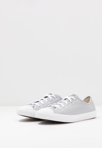 Szare płócienne trampki z białymi gumowymi podeszwami i noskami, z białymi sznurowadłami i minimalistycznym designem. Odpowiednie do codziennego noszenia.