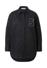 Camicia nera a maniche lunghe con bottoni, realizzata in tessuto liscio. Presenta una grande "S" bianca ricamata sul petto e un'orlo curvo.