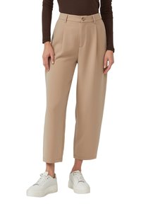 Beige maßgeschneiderte Hose mit hoher Taille, vorderen Abnähern und Seitentaschen, kombiniert mit weißen Plateau-Sneakern. Glatte Textur und strukturierter Schnitt.