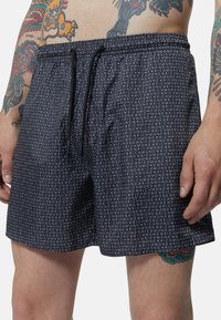 Pantaloni da bagno neri con un motivo ripetuto di testo bianco "RICHMOND", vita elastica e coulisse regolabile. Tessuto dalla consistenza liscia.