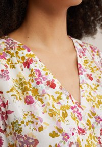 Tessuto a fantasia floreale con tonalità di rosa, giallo e verde. Design a V con dettaglio a bottone e una texture morbida e leggera.