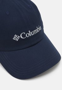 Sötétkék baseball sapka, textilből készült; ívelt napernyővel és varrott díszítéssel rendelkezik. A „Columbia” logó fehér színben található az elején.