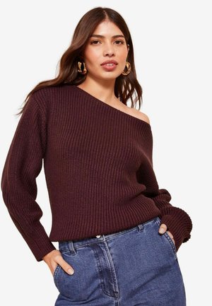 Burgundijas off-shoulder adīta džemperis ar ribotu tekstūru un garām piedurknēm, apvienots ar augstām jostasvietām džinsa biksēm.