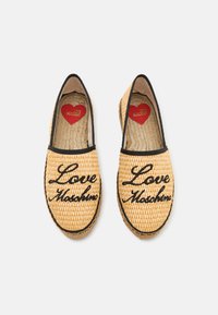 Espadrile din paie împletite, cu broderie neagră ce include textul "Love Moschino", un contur negru și un logo în formă de inimă pe o talpă interioară bej.
