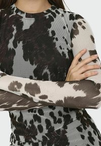 Haut à manches longues en tissu texturé affichant un motif de tache de vache noir et marron, avec un col rond et une silhouette cintrée.