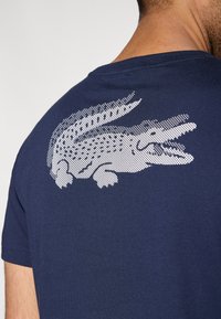 Granatowy t-shirt z krótkim rękawem, z białym nadrukiem krokodyla na górnej części pleców, ozdobionym wzorem z kropek.