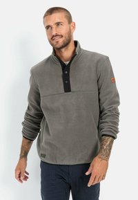 Grå fleecepullover med en sort placket, tre knapper og et mærke på venstre ærme. Har en kvart-længde lynlås og struktureret stof.