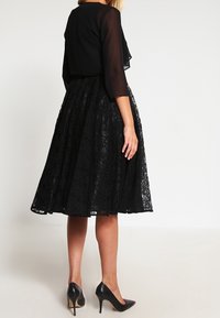 Czarna koronkowa sukienka z prześwitującym, krótkim czarnym topem. Rozkloszowana spódnica z teksturowanym kwiatowym wzorem. Do tego czarne szpilki.