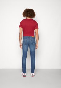 Blå jeans med rett passform, med en lys lærlapp bak i livet, kombinert med en kort rød t-skjorte og hvite sneakers.