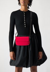 Black ribbed long-sleeve top with button details, paired with a black voluminous skirt. A bright pink rectangular handbag with stitching accents.