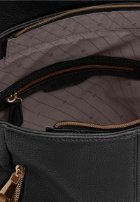 Intérieur d'un sac en cuir noir texturé avec un revêtement en tissu lisse et sombre, comportant une poche zippée et un compartiment. Accents en matériel doré visibles.