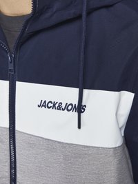 Mornarsko plava i bijela zip-up dukserica sivoj naglaskom, koja ima kapuljaču s nizom i logo "JACK & JONES" na prsima, u sportskom dizajnu.
