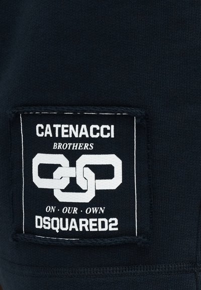 Patch en tissu noir avec un graphique de chaîne blanche entrelacée et le texte : « CATENACCI BROTHERS ON OUR OWN DSQUARED2 ».