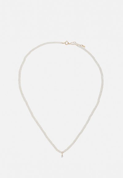 Pērļu kaklarota ar divām virkēm, kurā ir mazas baltas pērles un zelta aizdare. Viena pilienveida piekariņa pievieno akcentu tuvumā centra.