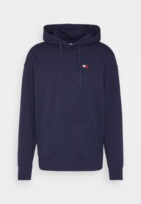 Navy blue hoodie made of cotton with a kangaroo pocket, adjustable drawstring, and a small logo patch on the chest. Standard fit.