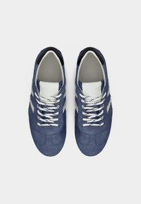 Ζευγάρι μπλε σουέντ αθλητικά παπούτσια με λευκά κορδόνια και λευκές ζιγκ-ζαγκ ρίγες, από ψηλά σε λευκό φόντο.