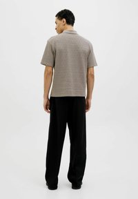 Ruskea lyhythihainen paitapusero, jossa on teksturoitu kuvio, yhdistettynä löysiin mustiin housuihin, esitetty takaa valkoista taustaa vasten.