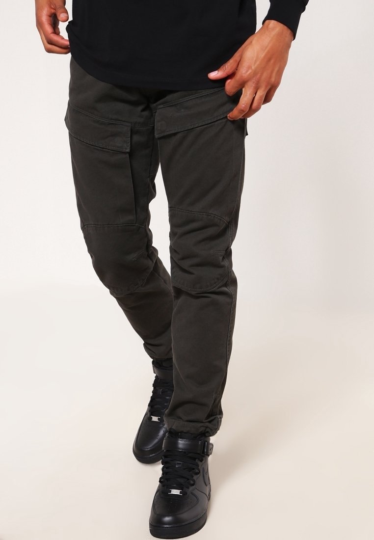 Cargo-byxor i mörkgrön tyg, med sidofickor, tapered fit och synlig söm. Matchat med svarta högklackade sneakers.