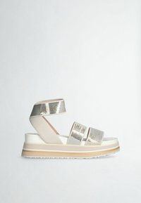 Sandale à plateforme beige avec trois brides perforées, dont une autour de la cheville, et une semelle épaisse rayée.