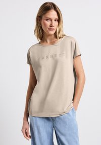Beige tričko s krátkým rukávem s nápisem "CONNECT" z kamínků na hrudi, volný střih, hladká textura a kulatý výstřih.